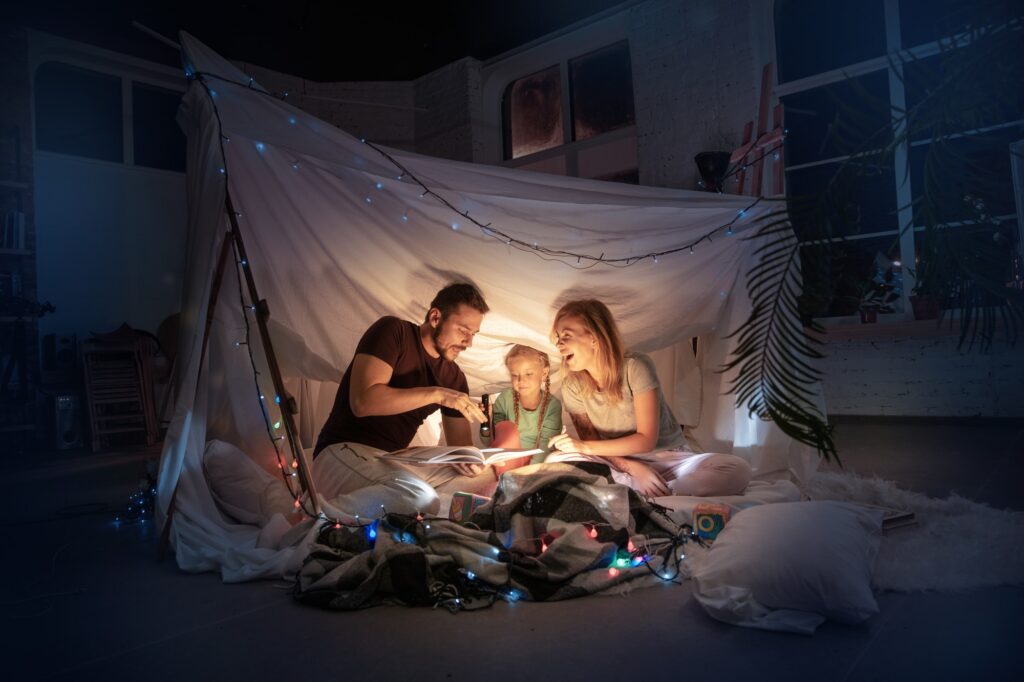 Family sitting in a teepee, reading stories with the flashlight