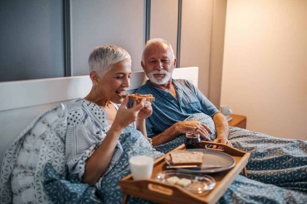 Older man and woman eating in bed