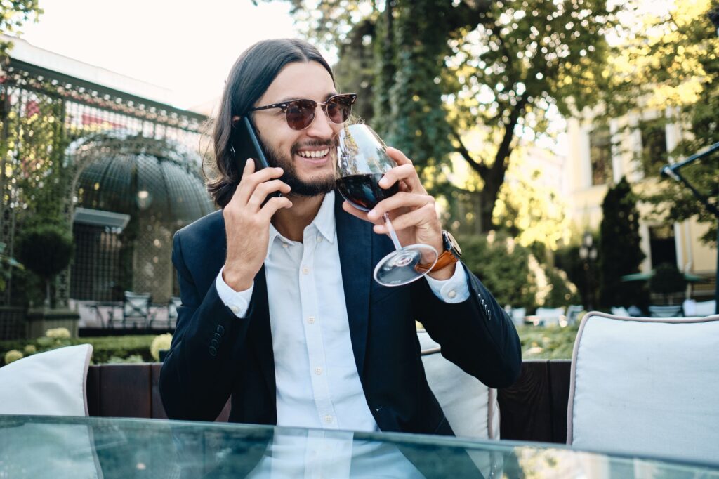 Rich smiling latin man happily talking on cellphone drinking wine resting in restaurant outdoor