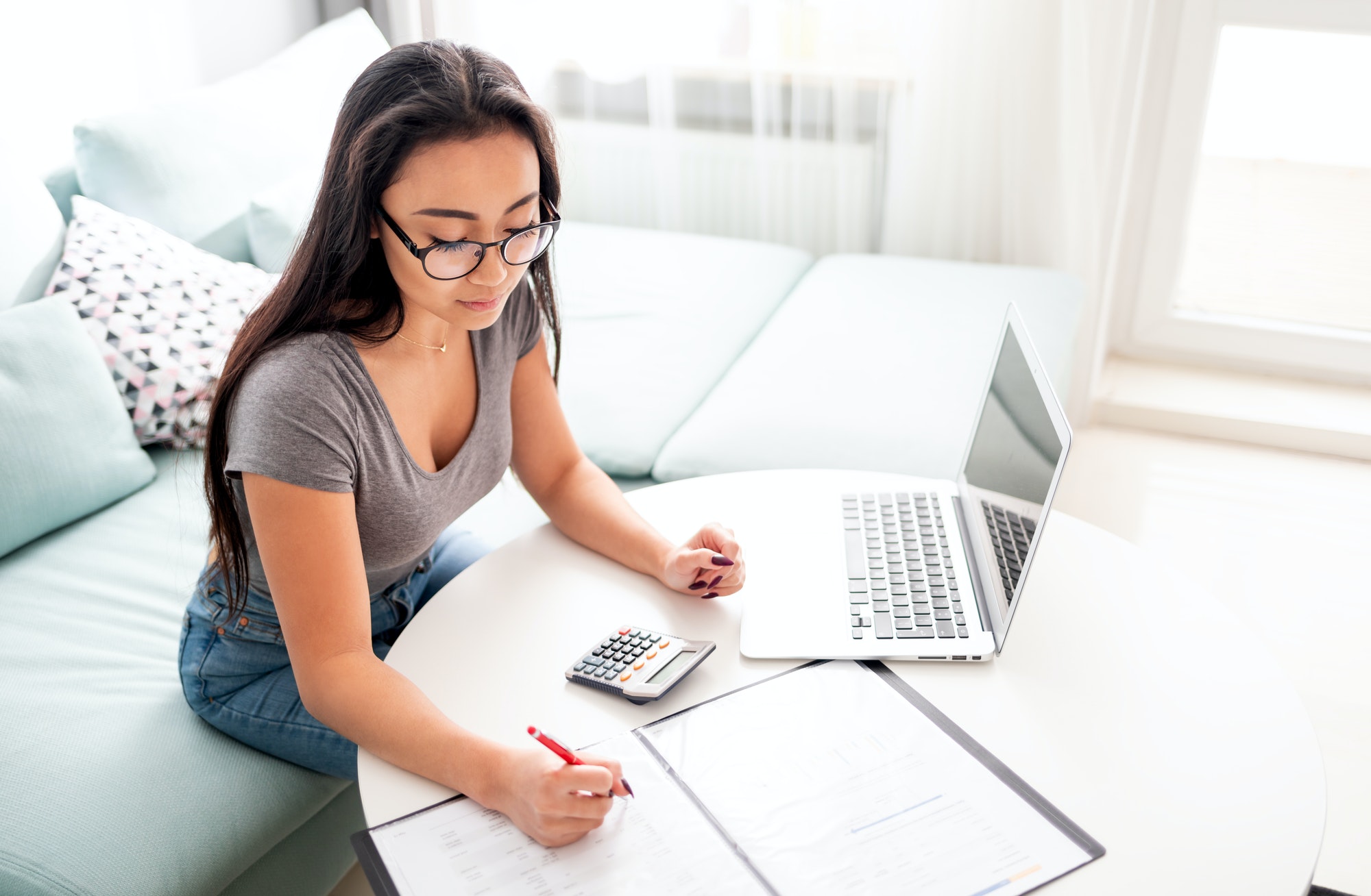 Asian woman using calculator and laptop for calaulating home budget finance taxes