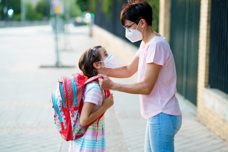 Mother preparing her little girl for the return to school wearing a mask