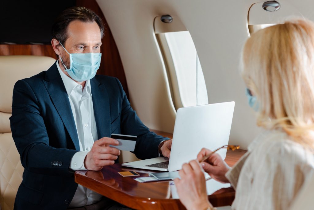 Selective focus of businessman in medical mask holding credit card and using laptop near